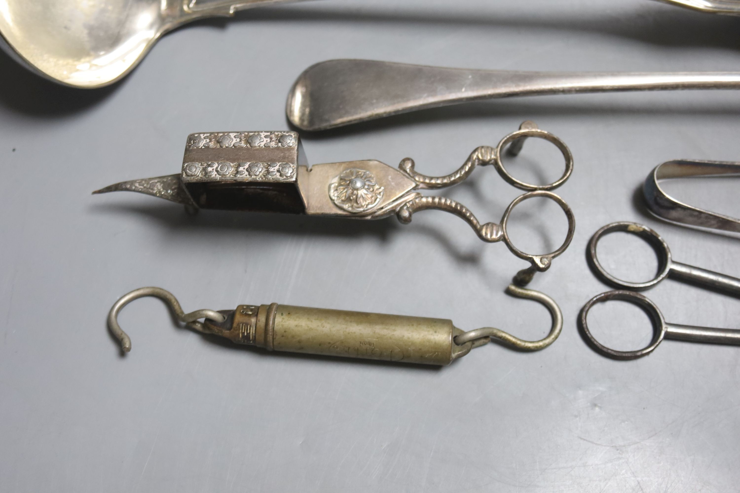 A large plated ladle and basting spoon, two candle snuffers, tongs and spring balance